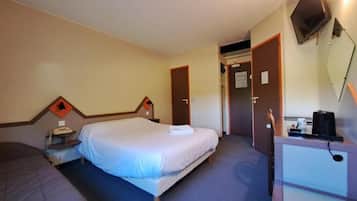 A hotel room with a single bed, a desk with a computer, a telephone, and a television.