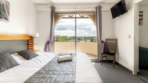 A hotel room with a bed, a chair, a TV, and a balcony with a view.