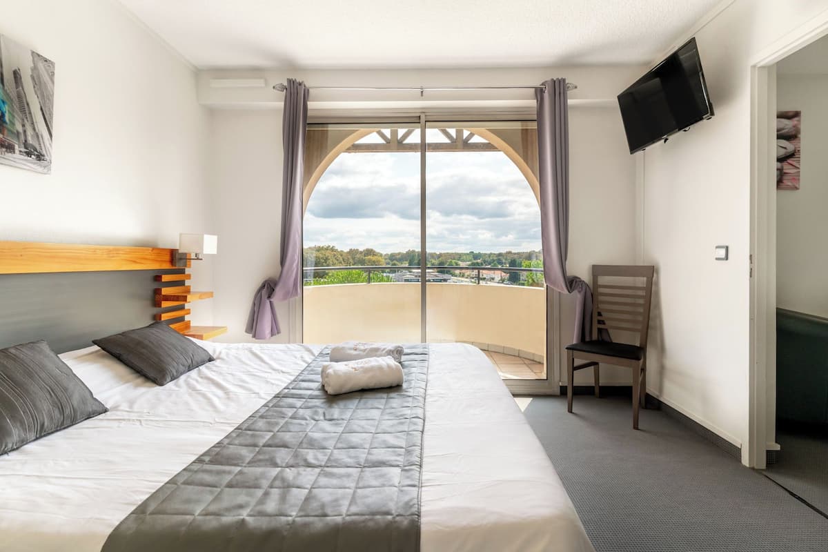 A hotel room with a bed, a chair, a TV, and a balcony with a view.