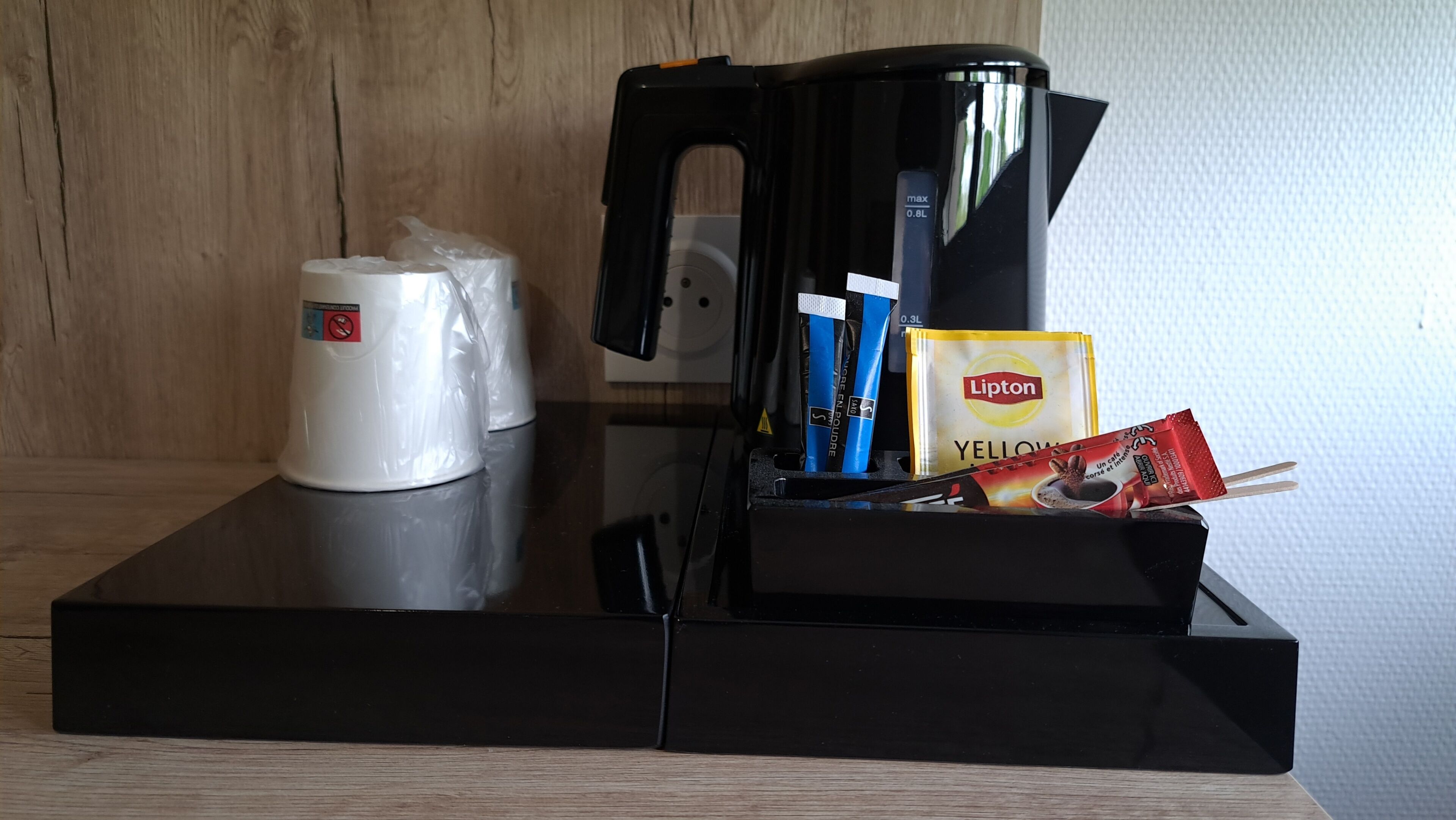 A coffee machine, a white cup, and Lipton tea packets on a tray.