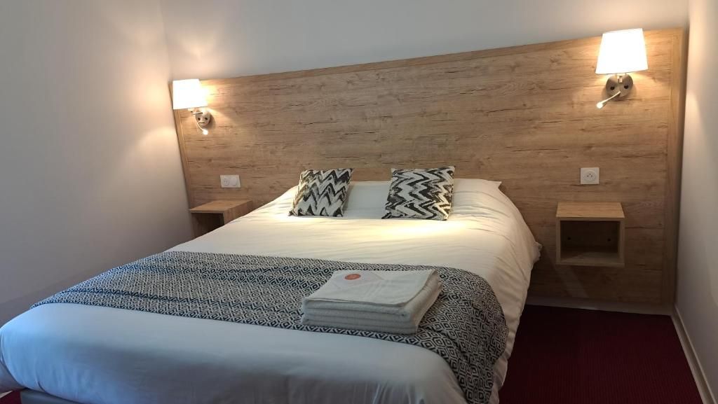 A hotel room with a wooden headboard, two bedside lamps, a bed with patterned bedding, and a red carpet.