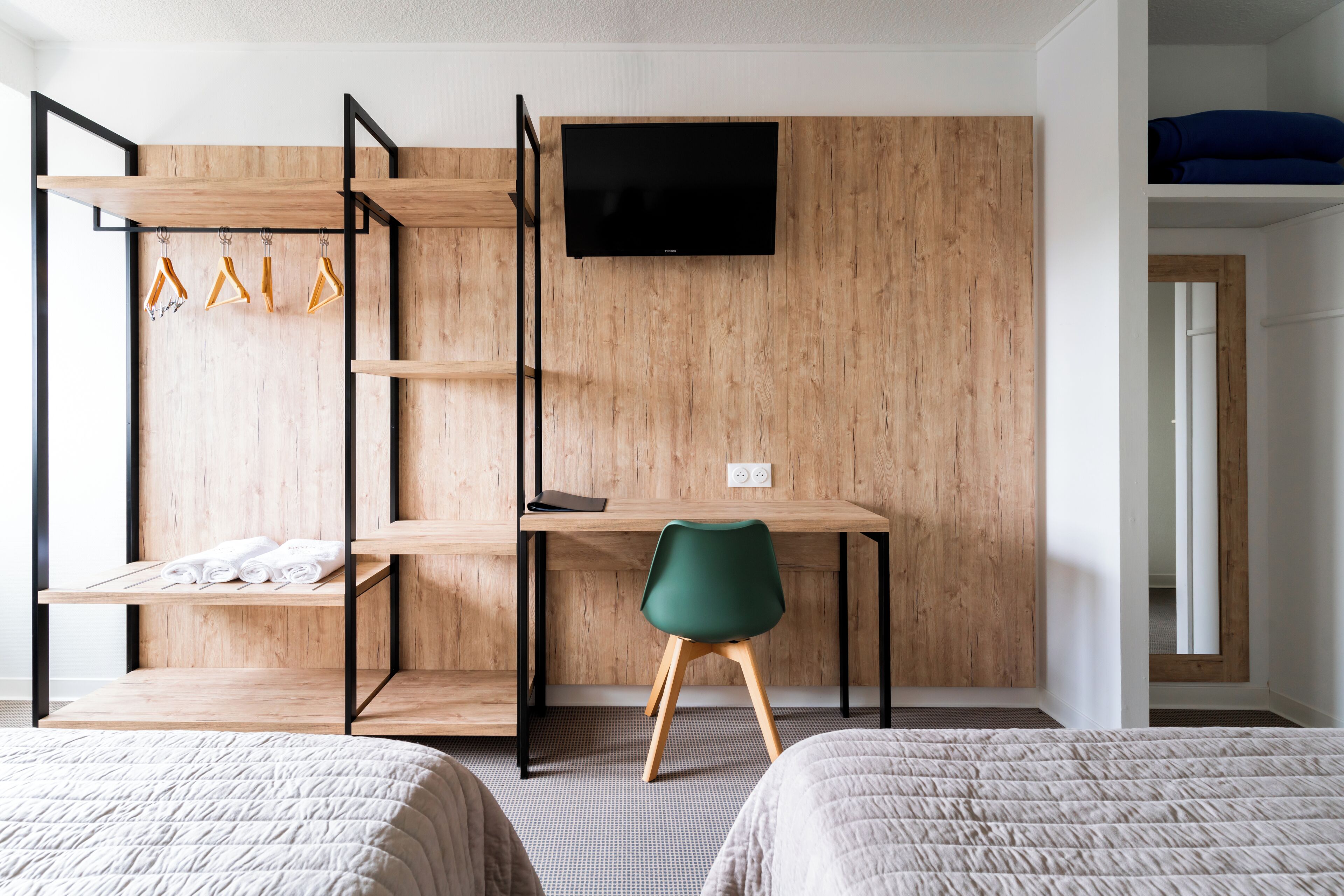 A room with a bed, a desk, a chair, a TV, and a wardrobe with clothes and hangers.