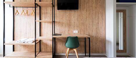 A room with a bed, a desk, a chair, a TV, and a wardrobe with clothes and hangers.