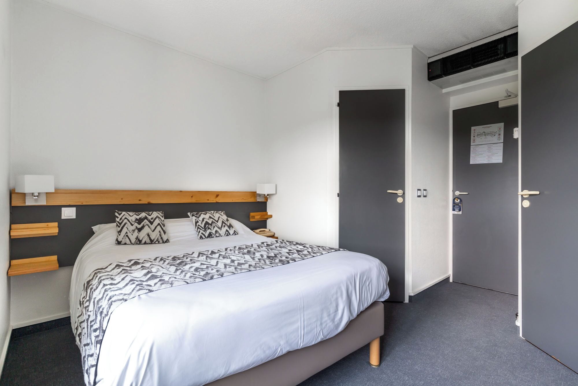 A bedroom with a bed, bedside lamps, a headboard, and a door.