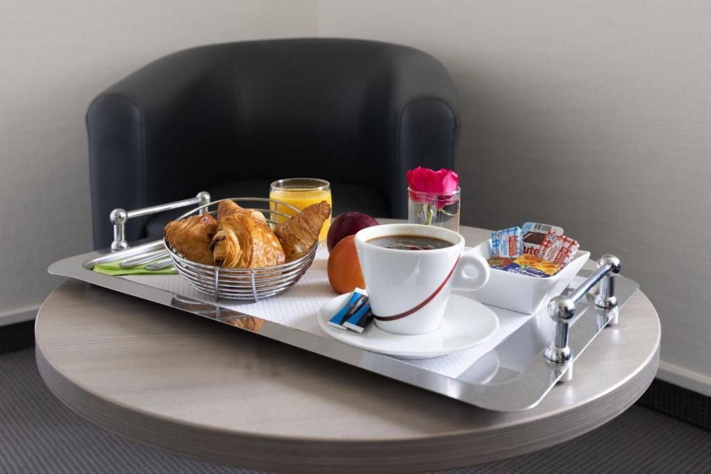 Bandeja de desayuno con cruasanes, jugo de naranja, café y un pequeño florero con una flor.