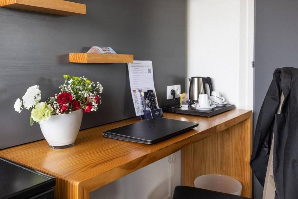A hotel reception desk with a laptop, a coffee machine, a telephone, and a flower arrangement.