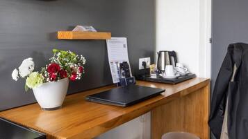 A hotel reception desk with a laptop, a coffee machine, a telephone, and a flower arrangement.