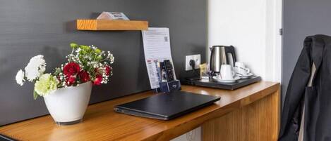 Un mostrador de recepción de hotel con una computadora portátil, una máquina de café, un teléfono y un arreglo floral.