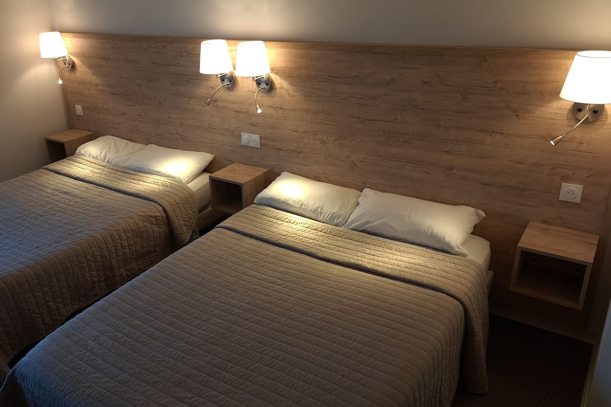 A hotel room with two beds, each with a wooden headboard and bedside lamps.