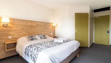 Habitación de hotel con cabecera de madera, cama con colcha estampada, dos lámparas de noche y una mesita de noche de madera.