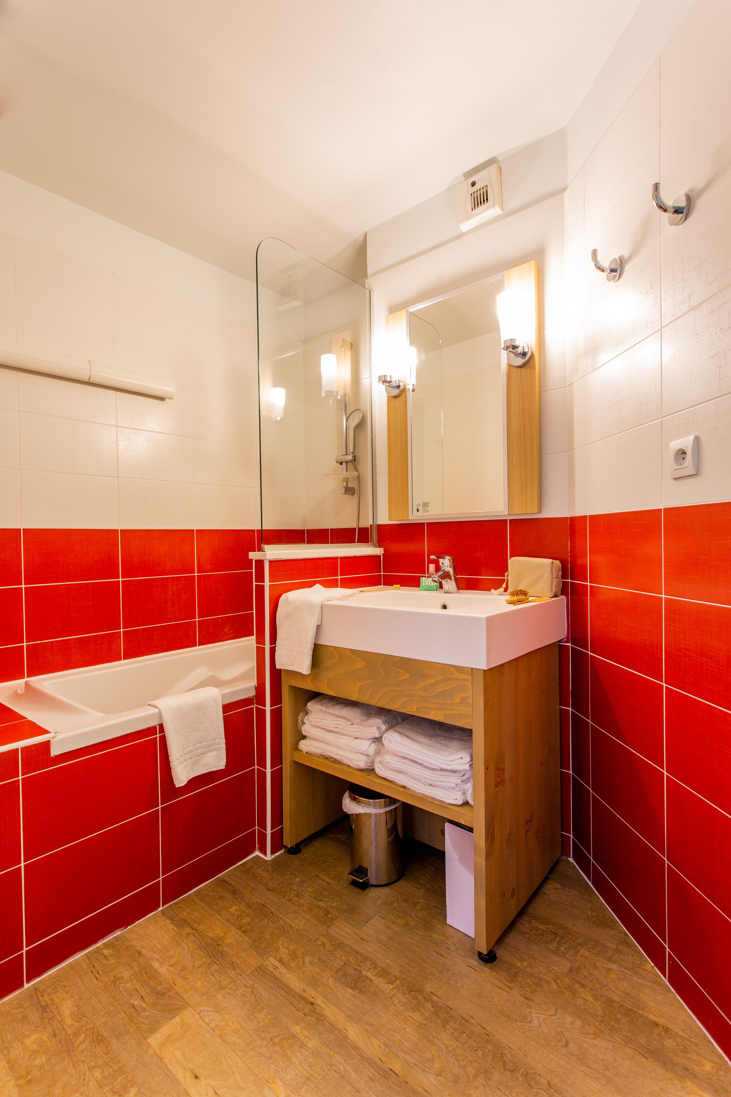 A bathroom with a white sink, red-tiled walls, a wooden vanity, a glass shower enclosure, and a white bathtub.