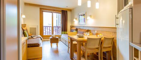 A modern kitchen with wooden flooring, a dining table with chairs, a built-in oven, and a refrigerator.