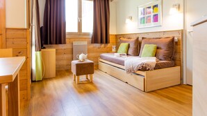 A cozy room with a wooden bed, a small table, a chair, and a window with curtains. - Residence Pierre & Vacances Les Gemeaux (La Plagne-Tarentaise)