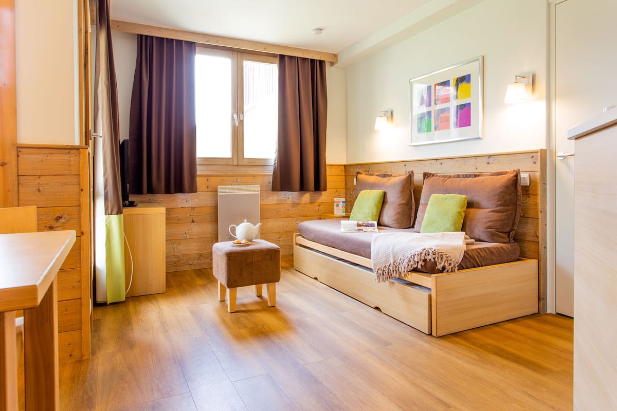 Una habitación acogedora con una cama de madera, una mesita, una silla y una ventana con cortinas.