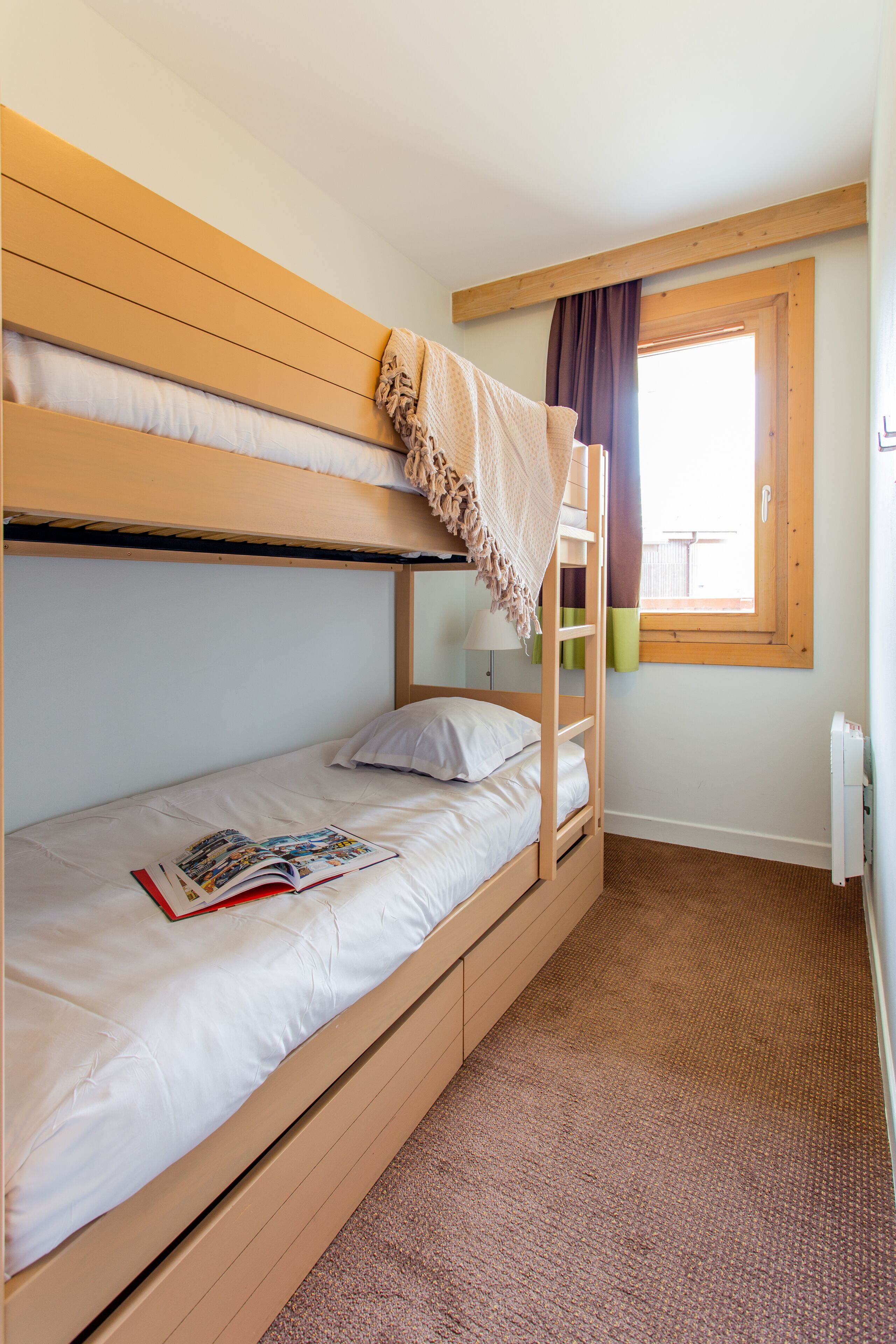 A bunk bed room with a window, a lamp, and a radiator.