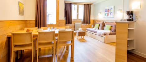 A modern hotel room with a wooden dining table, chairs, a sofa, and a coffee machine.