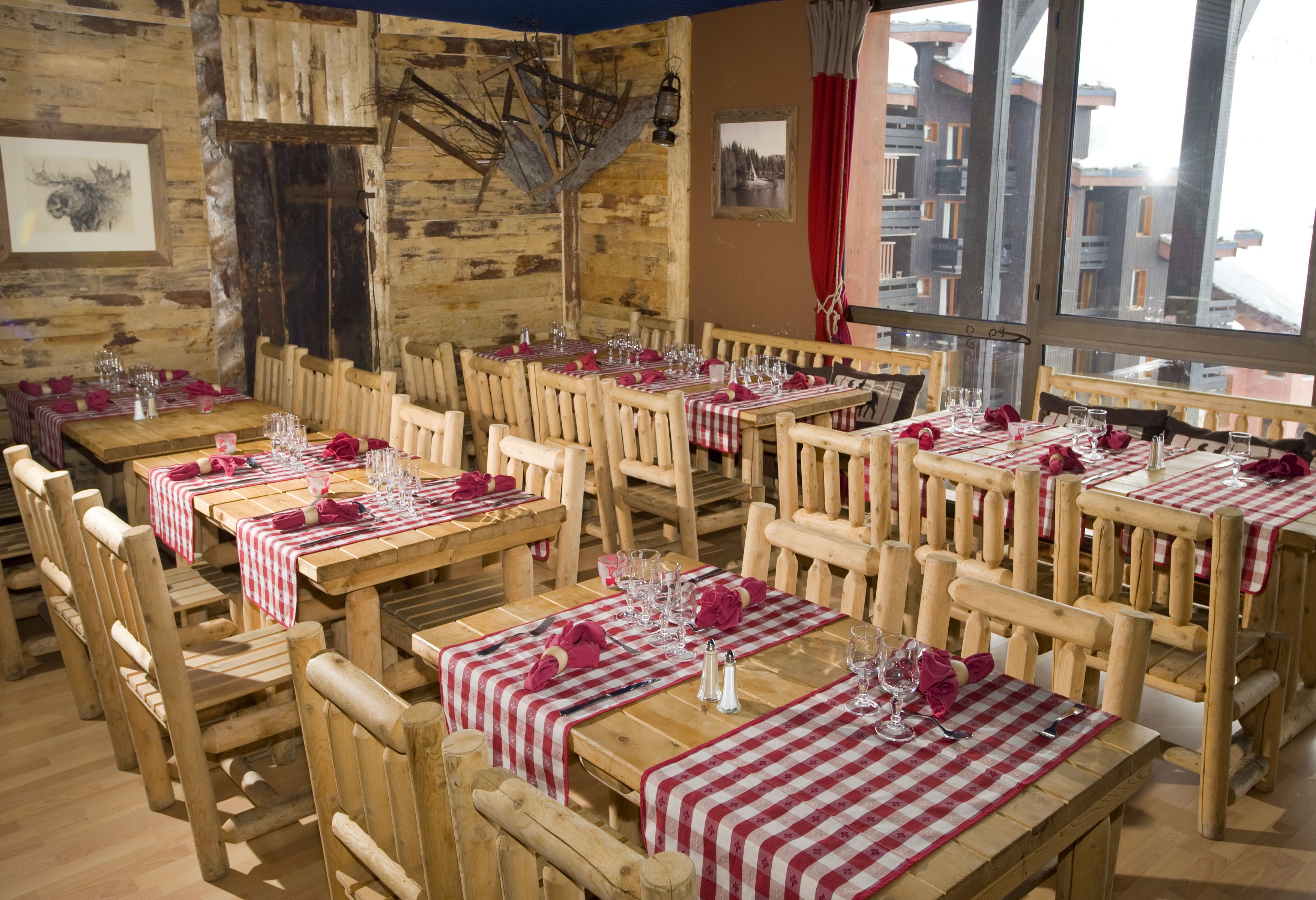 Un restaurant avec des tables et des chaises en bois, des nappes à carreaux rouges et blancs, et un décor rustique.
