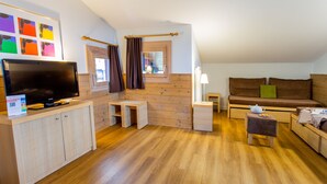 A compact living space with a TV, wooden furniture, a small table, a sofa, and a window with curtains. - Residence Pierre & Vacances Les Gemeaux (La Plagne-Tarentaise)