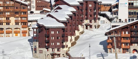 En snötäckt bergsanläggning med flervåningsbyggnader, skidliftar och en parkeringsplats.