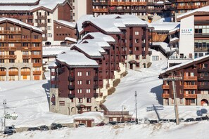 Une station de montagne enneigée, avec des bâtiments à plusieurs étages, des remontées mécaniques et un parking.