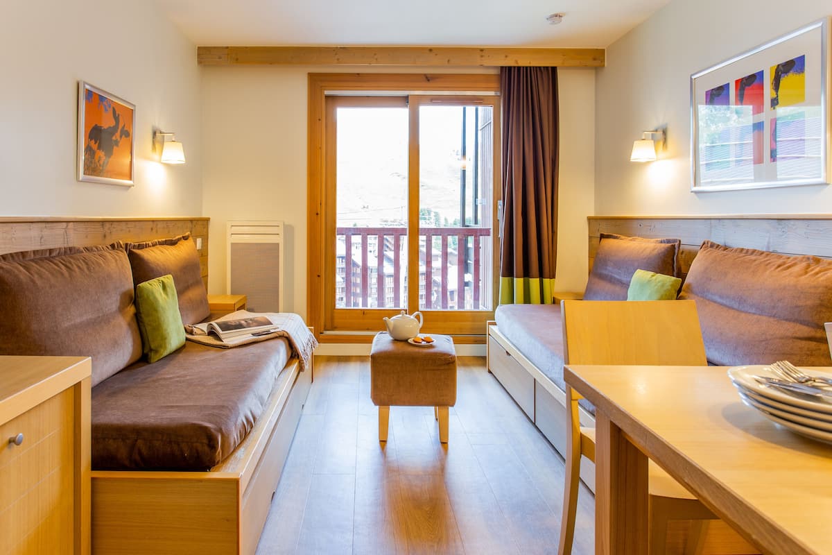 Una habitación acogedora con cabecera de madera, un sofá, una mesa con cubiertos y una ventana con vistas a edificios.