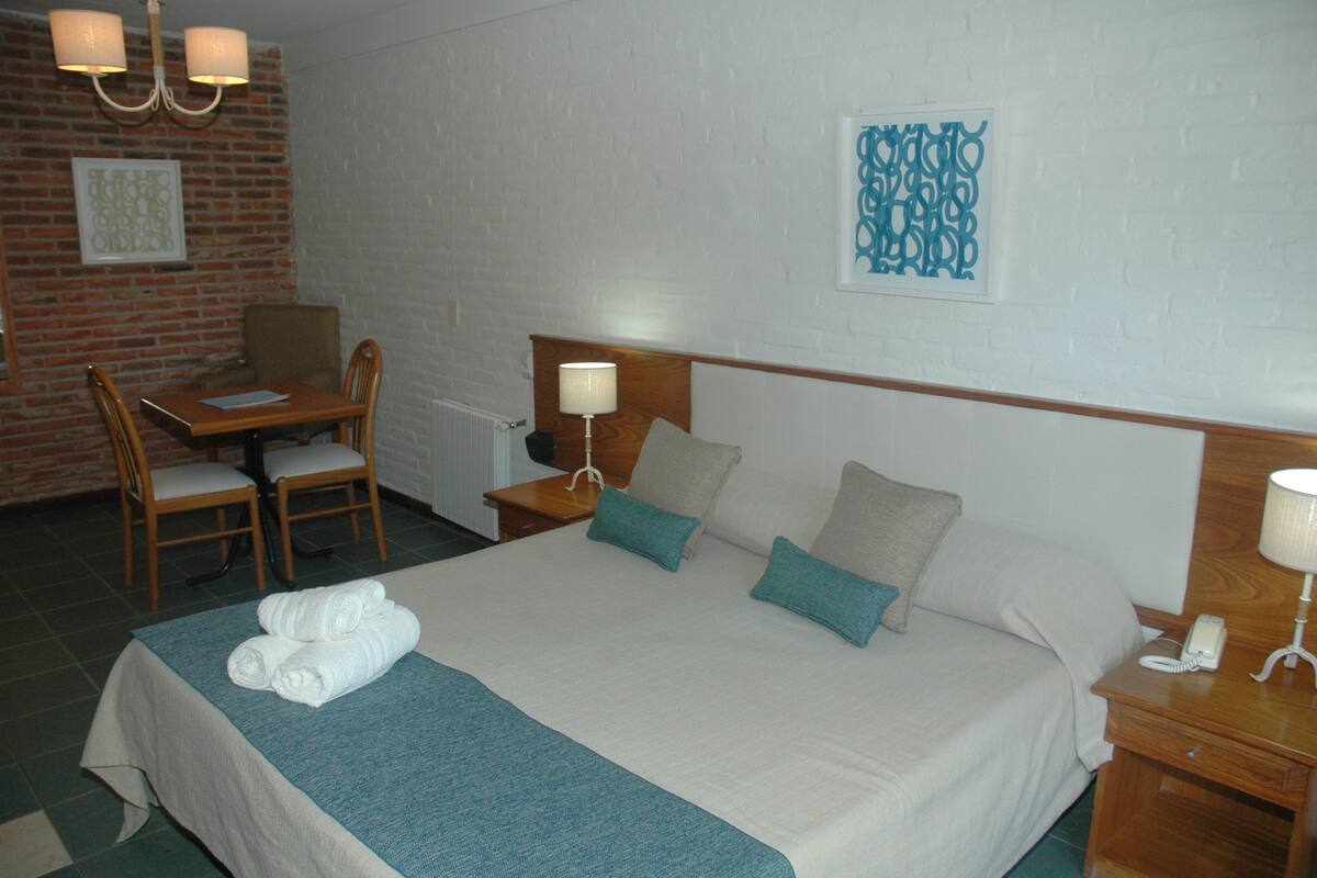 Una habitación de hotel con una cama, dos sillas, un escritorio, una lámpara y un teléfono.
