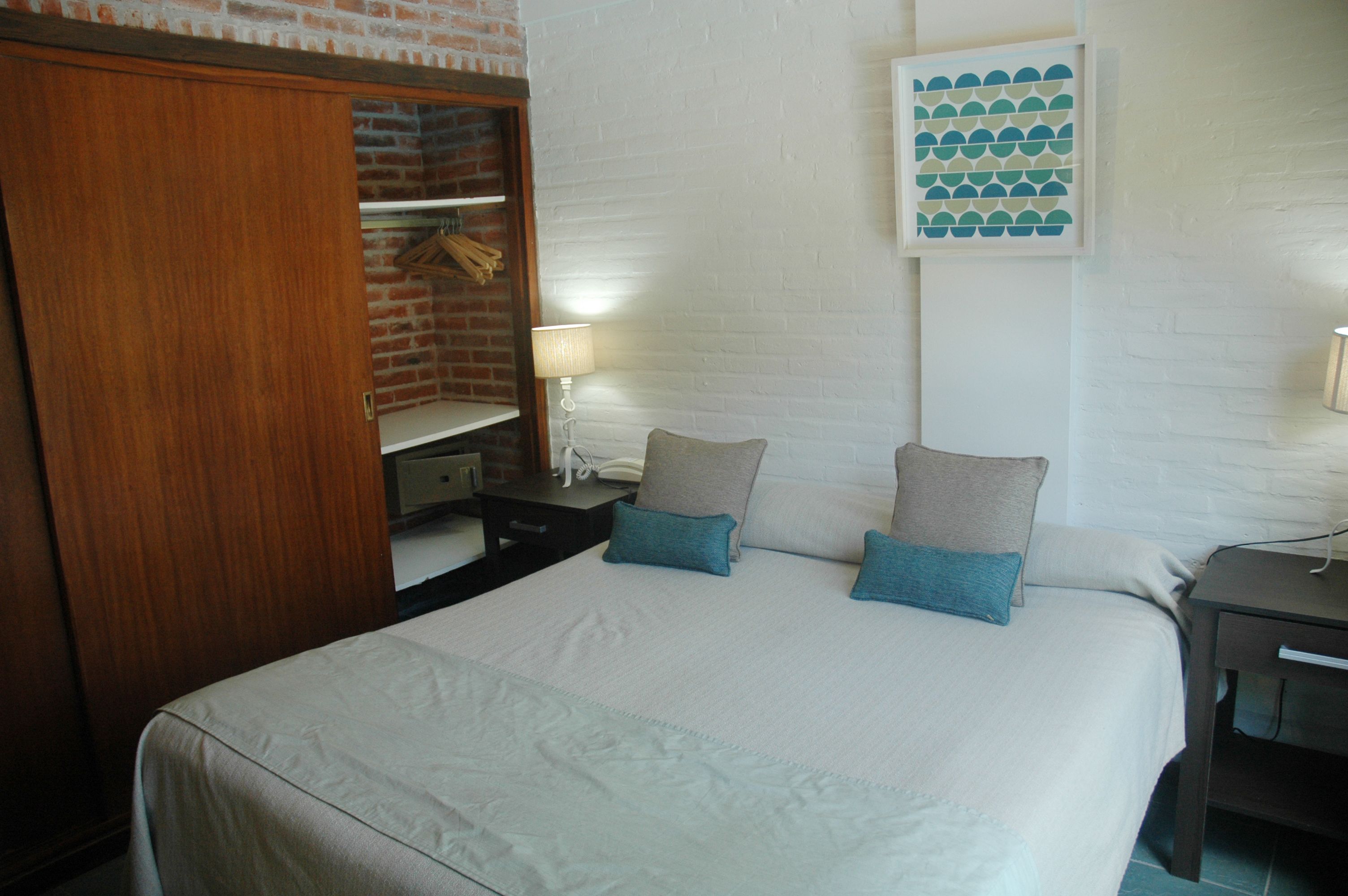 A hotel room with a bed, a wardrobe, a desk, and a wall-mounted artwork.