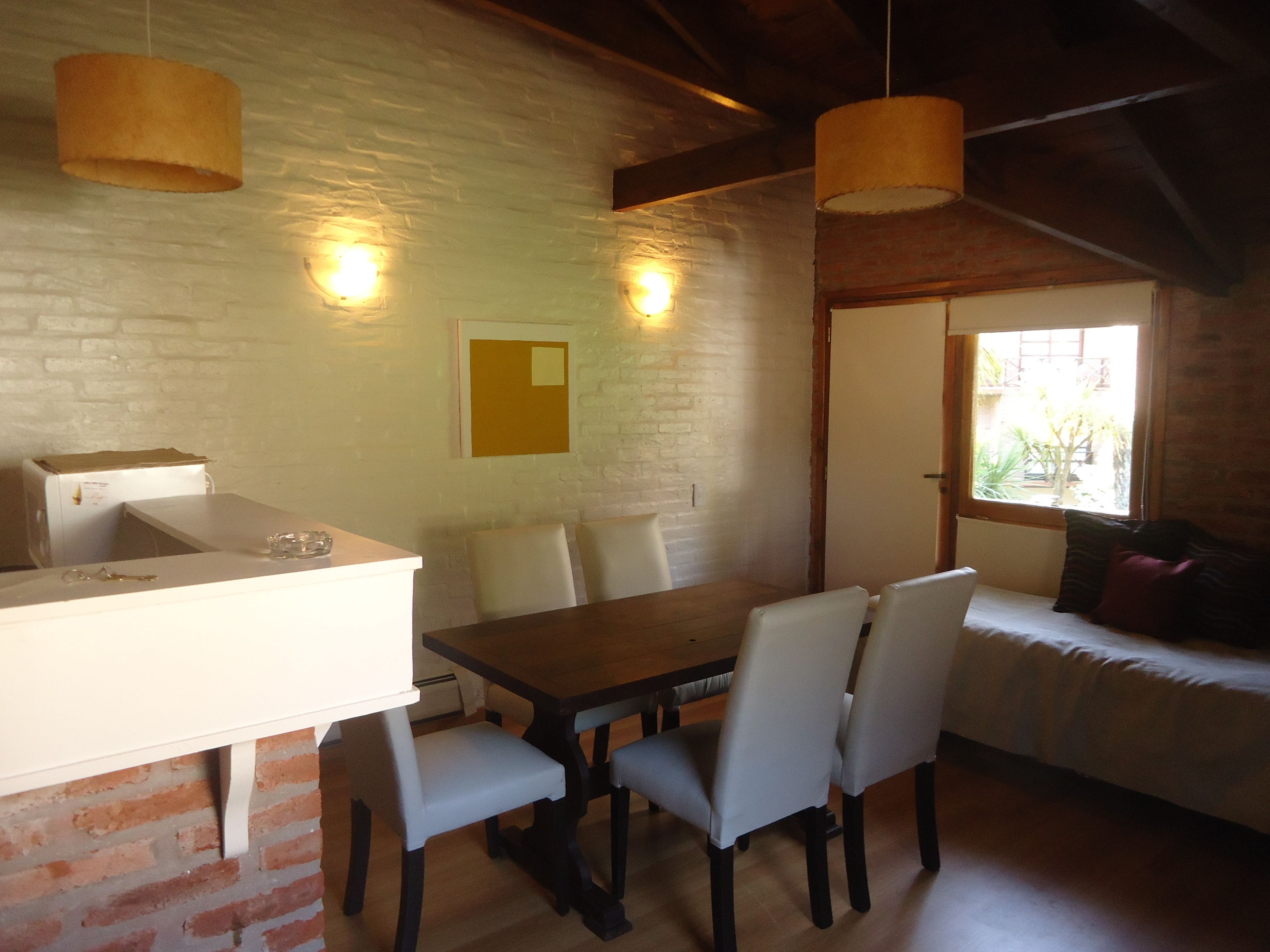 A dining area with a wooden table and chairs, a white counter, and a brick wall.