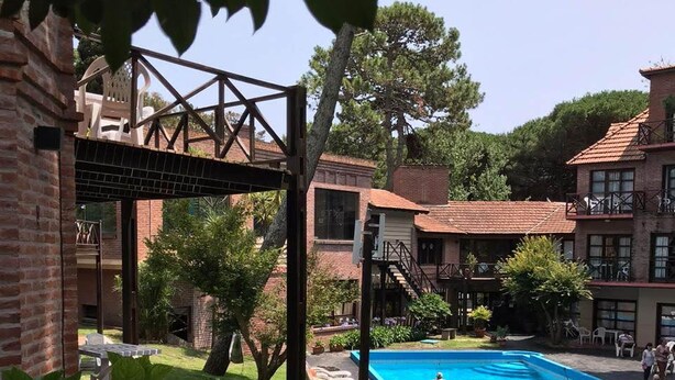 A pool area with a clear blue pool, surrounded by brick buildings and greenery. - Australis Paradise (Carilo)