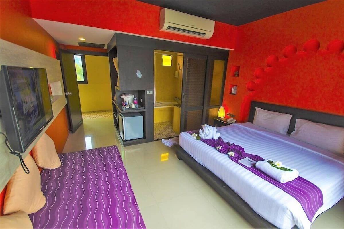 A hotel room with a bed, a desk, a TV, and a bathroom visible through an open door.
