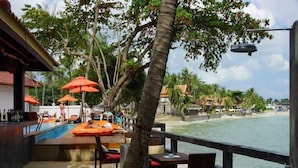 Un bar frente a la playa con terraza, sombrillas y vista al océano.