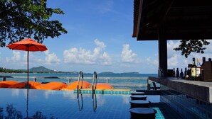 Una piscina infinita con vista al mar, sillas de descanso anaranjadas y una zona de bar con botellas.