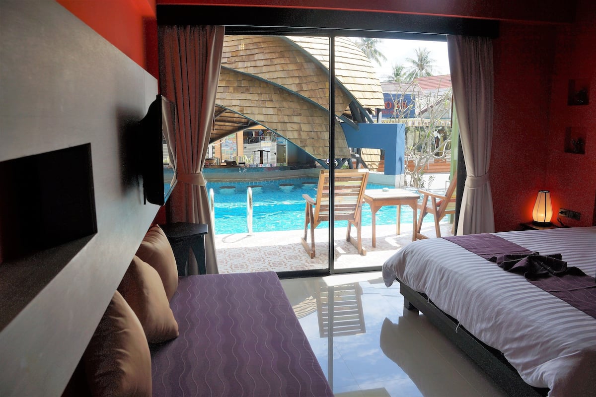 A hotel room with a bed, a sofa, a pool view, and a table with chairs.