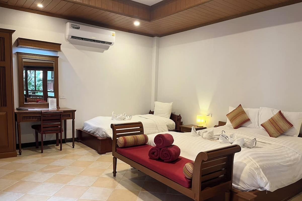A hotel room with two beds, a desk, and an air conditioning unit.