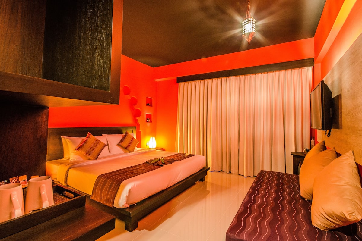 A hotel room with a large bed, bedside tables, a bedside lamp, a TV, a window with curtains, and a wooden headboard.