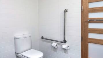 A small, modern bathroom with white tiles, a white toilet, a grab bar, and a wooden door with frosted glass panels.