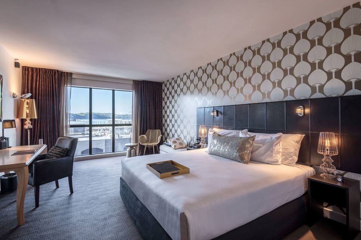 A hotel room with a large bed, a desk, a chair, and a view of the cityscape.