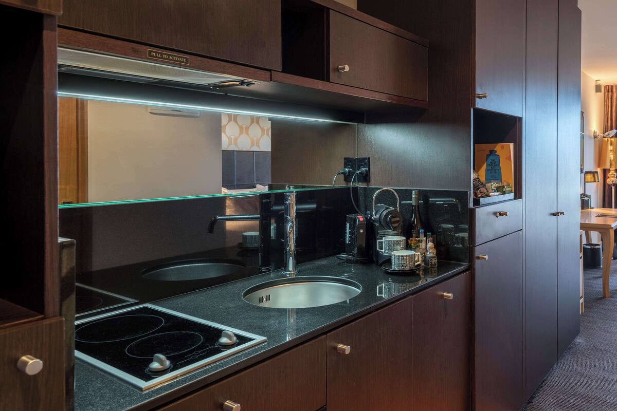 A compact kitchen with a gas stove, two sinks, a coffee machine, and a wine bottle.