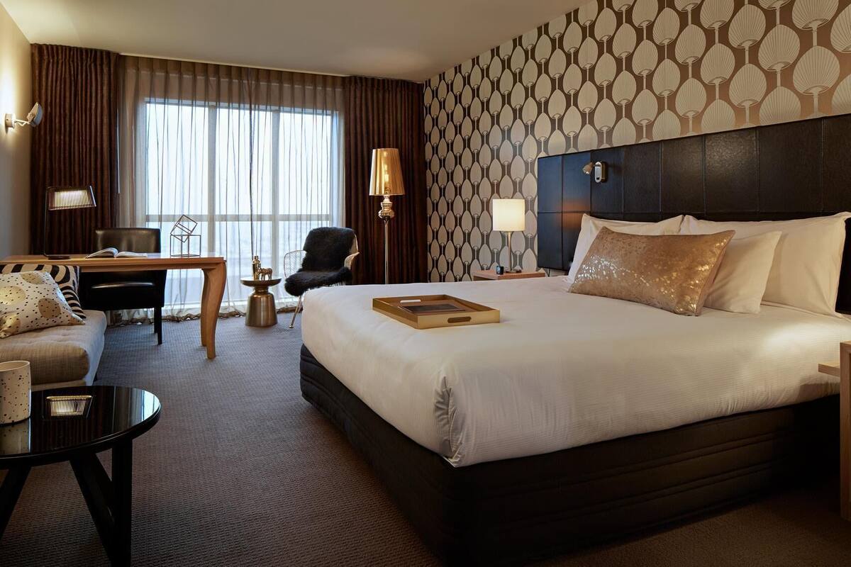 A hotel room with a large bed, a desk, a chair, and a small table.
