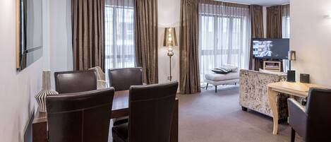 A modern hotel room with a dining area, a sofa, a TV, and a lamp.