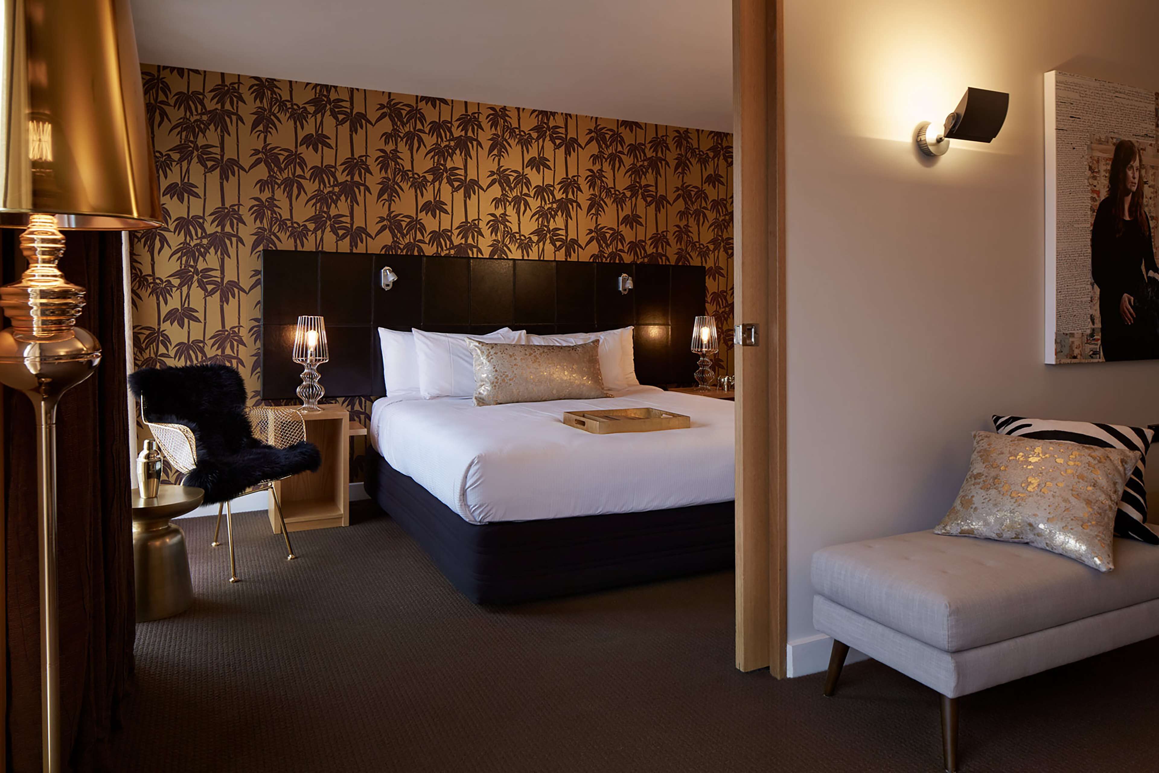 A hotel room with a large bed, a desk with a chair, a sofa, and a wall with a decorative pattern.