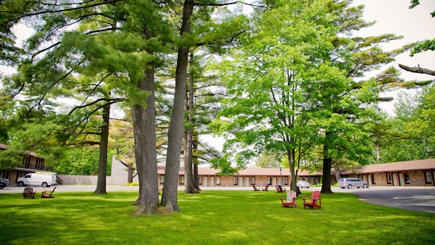 A motel with multiple rooms, a parking area, and a lawn with trees and benches.