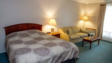 A hotel room with a bed, a chair, a table, and two lamps.