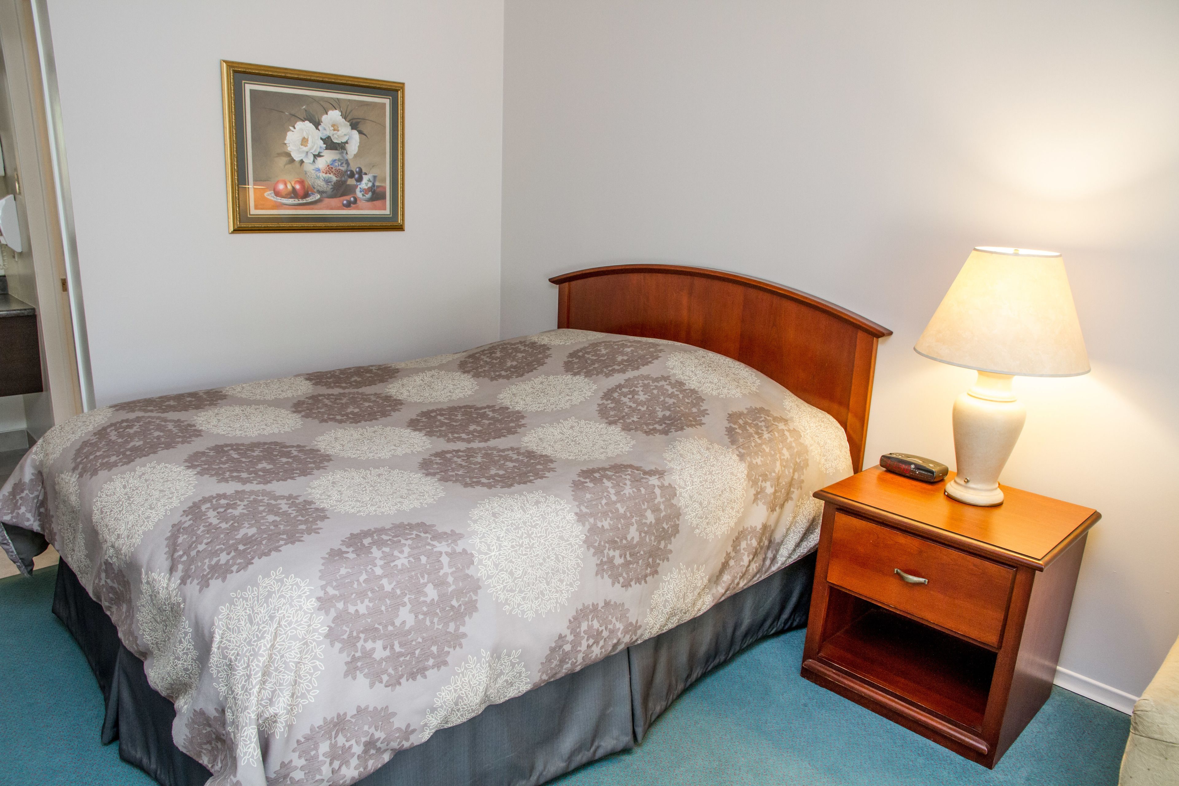 A bedroom with a bed, a nightstand with a lamp, and a framed picture on the wall.