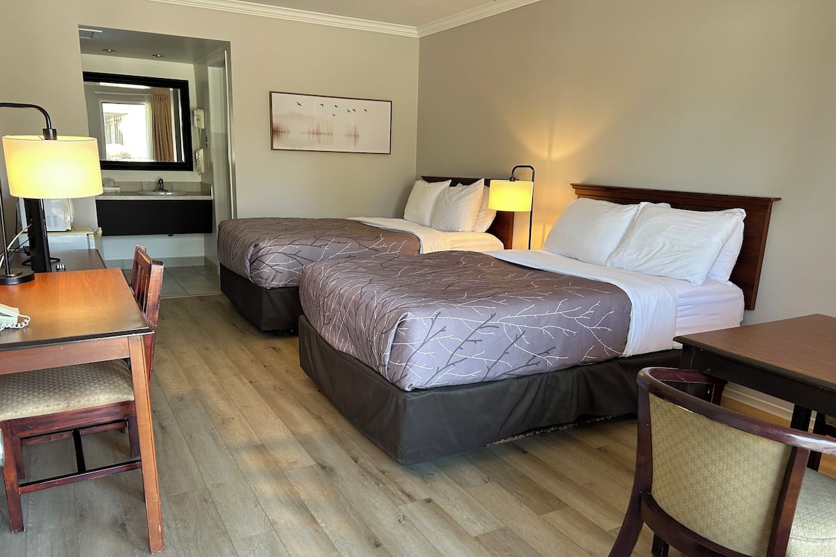 A hotel room with two beds, a desk, a chair, a lamp, and a painting on the wall.
