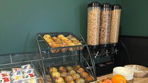 A breakfast buffet with various pastries, fruits, and cereal containers.
