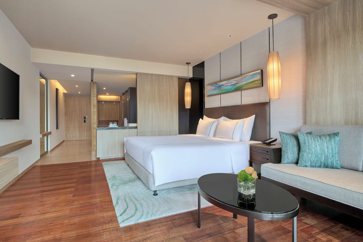 A modern hotel room with a large bed, a sofa, a flat-screen TV, and a dining area.