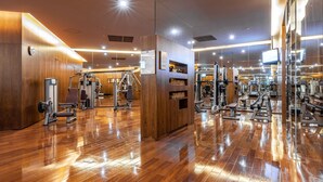 Un gimnasio moderno con piso de madera, diversos equipos de ejercicio y una amplia pared de espejos.