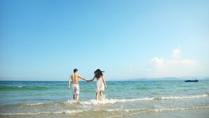 Una pareja caminando de la mano por una playa con aguas tranquilas y cielo despejado.