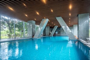 Une piscine intérieure avec des parois en verre transparent, un plafond en bois et de grandes colonnes en béton.